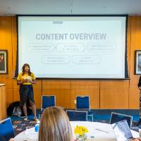 A woman presenting to a room full of people, projector reads "context overview"